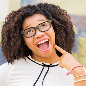 Woman smiling and pointing to teeth after same day dental crown treatment