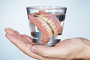 Hand holding dentures in a glass of water