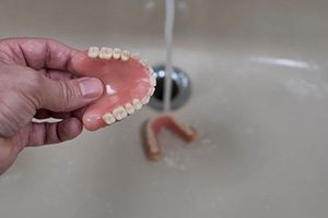 Person rinsing their dentures in the sink