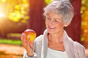 Older woman with dental implant supported replacement teeth eating an apple