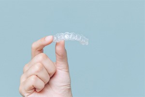 Hand holding Invisalign aligner against neutral background
