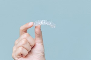 Hand holding Invisalign aligner against neutral background