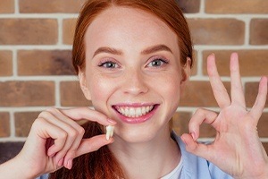 Young woman holding up her extracted wisdom tooth and smiling