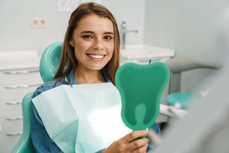 Woman at dentist’s office looking at smile in mirror