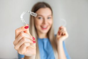 Smiling woman holding Invisalign aligner 